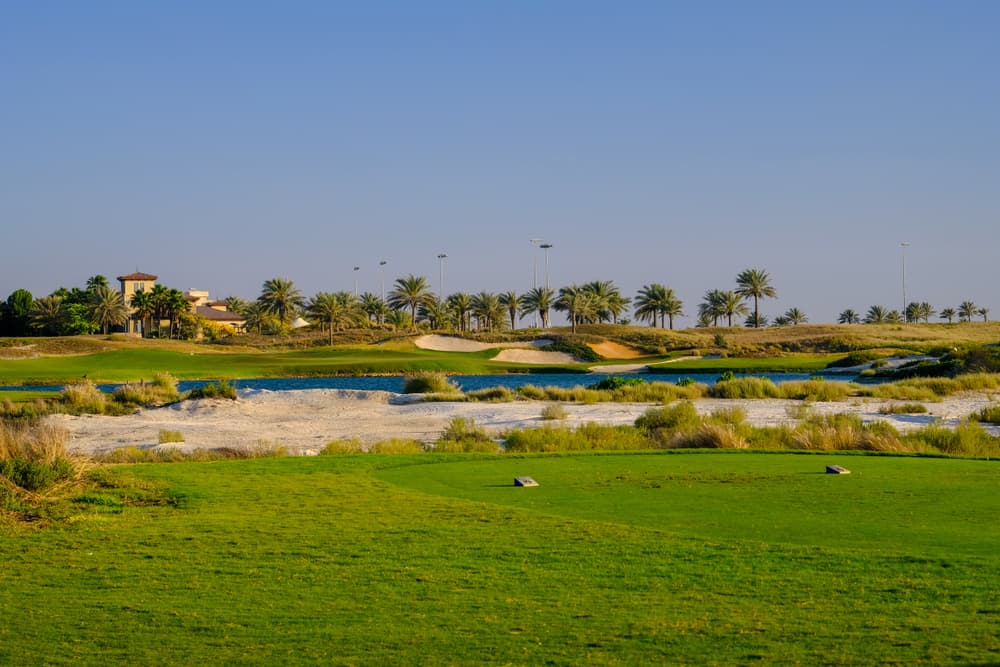 A tee looking across sandy waste areas and palms at Saadiyat Beach Golf Club at sunset